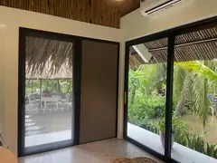 Cửa kính khung đen nhìn ra vườn, một cánh lắp rèm tổ ong màu nâu kéo ngang