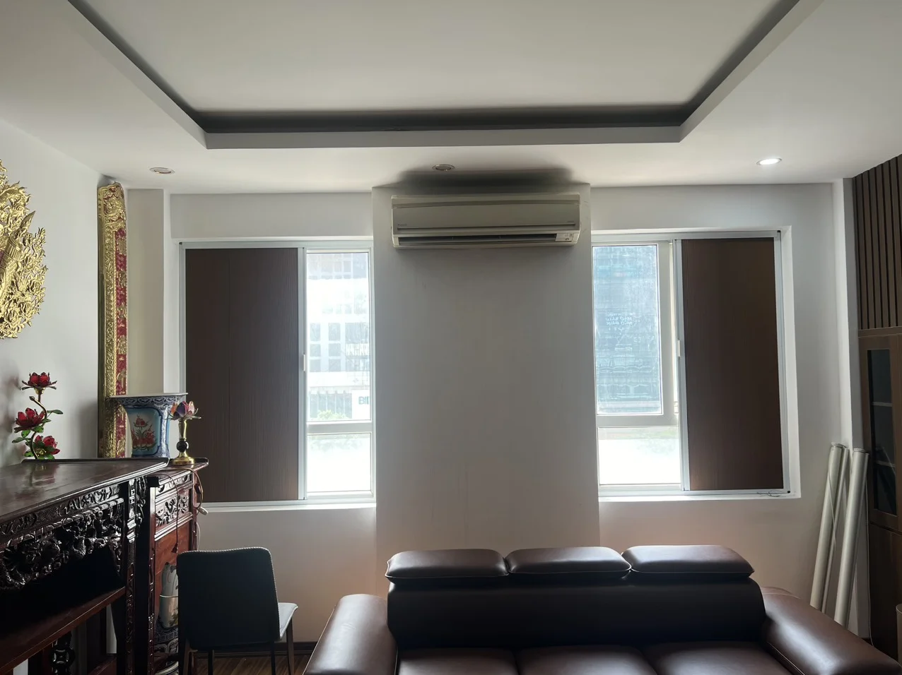 Phòng khách có hai cửa sổ lắp rèm màu nâu đậm hai bên máy điều hoà