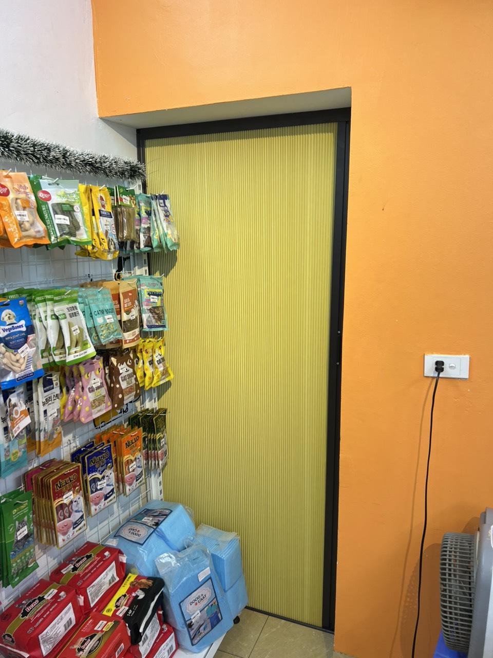 Rèm màu vàng nhạt khung đen lắp ở cửa đi cạnh kệ hàng