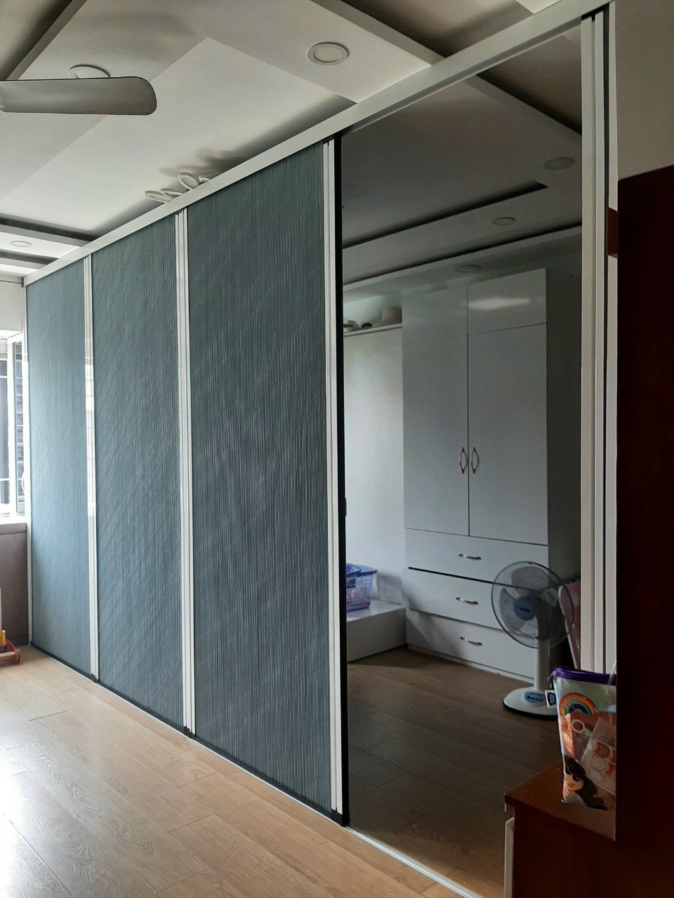 Vách ngăn ba cánh màu ghi xanh, mở một phần sang phòng ngủ có tủ trắng