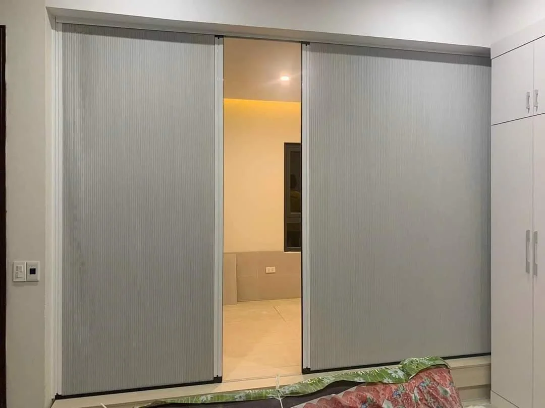 Vách ngăn màu ghi bạc hai cánh mở một lối vào phòng ngủ, bên cạnh tủ trắng