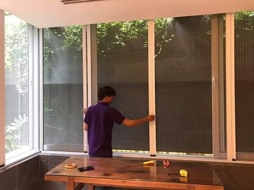 Thợ đang lắp cửa lưới chống muỗi dạng lùa cho dãy cửa sổ góc nhìn ra vườn