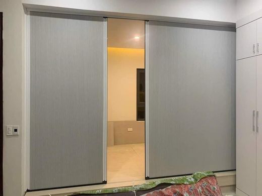 Vách ngăn màu ghi bạc hai cánh mở một lối vào phòng ngủ, bên cạnh tủ trắng